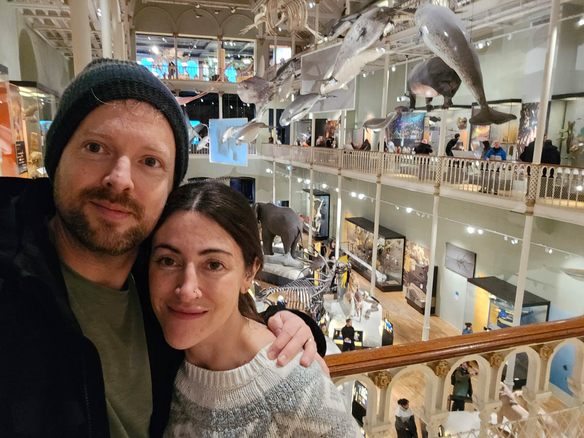 Chris and Janette taking a selfie overlooking the Animal World gallery with suspended marine creatures behind them