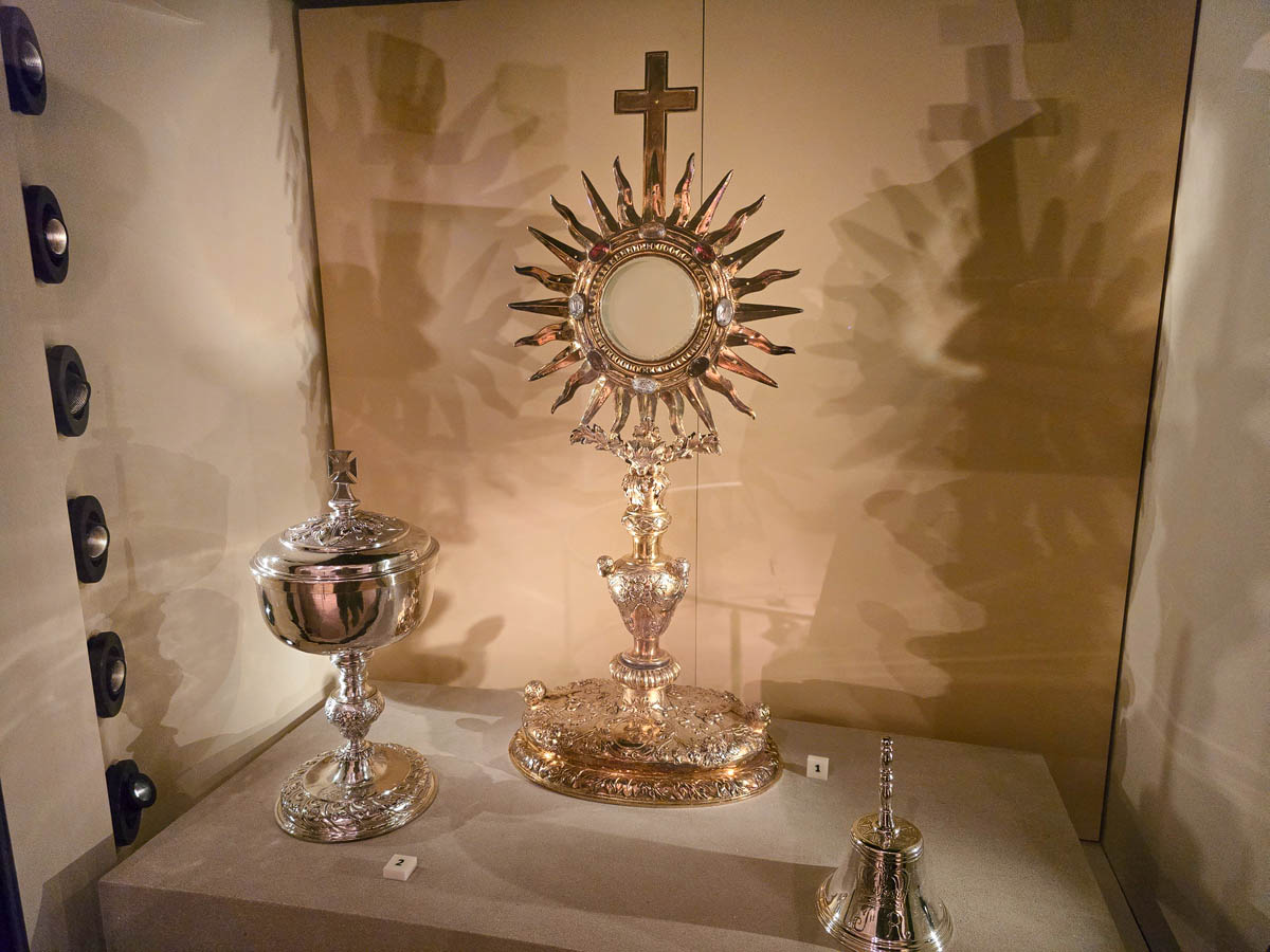 An ornate golden monstrance with sunburst design and a silver ciborium on display in the National Museum of Scotland