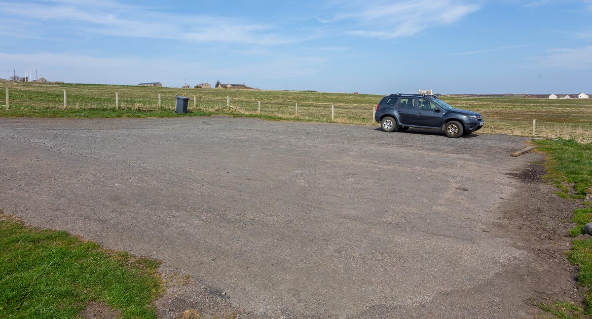 The small free car park at Nybster Broch with a single car and flat Caithness farmland stretching to the horizon