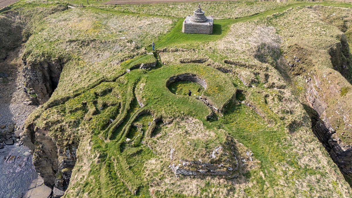 Drone view of Nybster Broch from the south showing the settlement ruins, Mervyn’s Tower and sheer cliff edges on the promontory