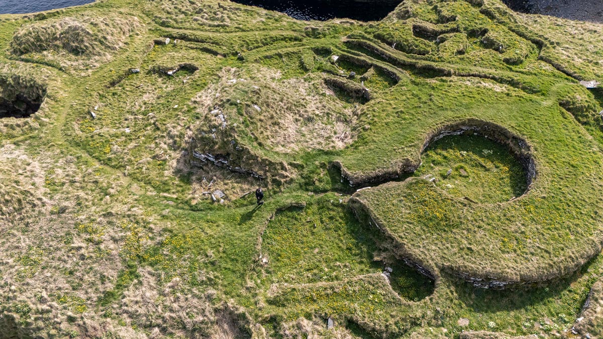 Aerial drone view of the seaward outbuildings at Nybster Broch showing circular cellular structures with a person for scale