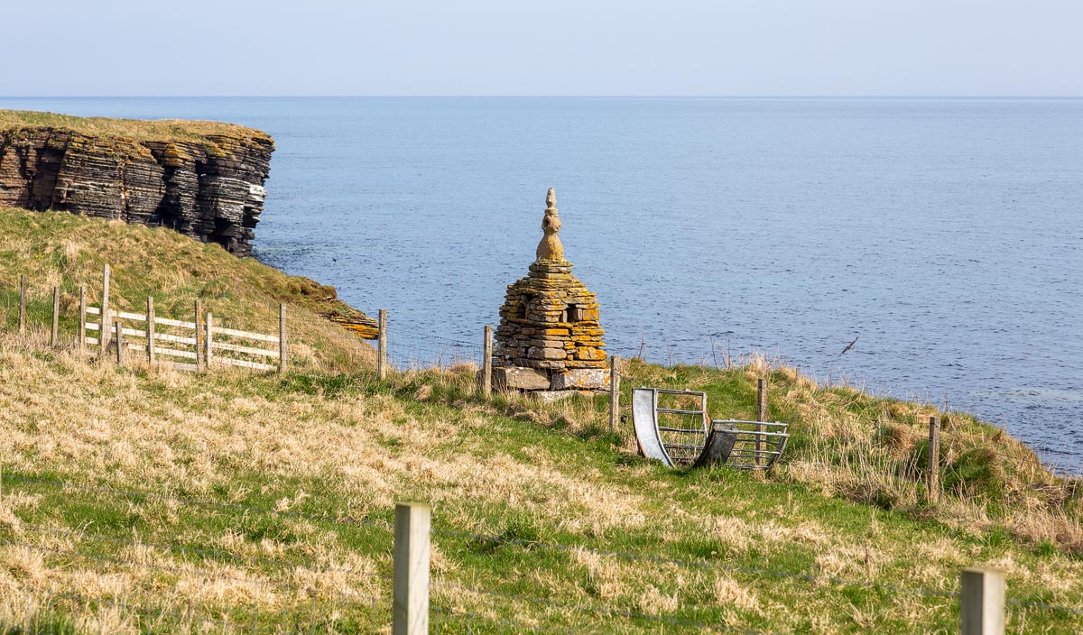 A small stone cairn monument on the clifftop near the Nybster Broch path with the North Sea beyond