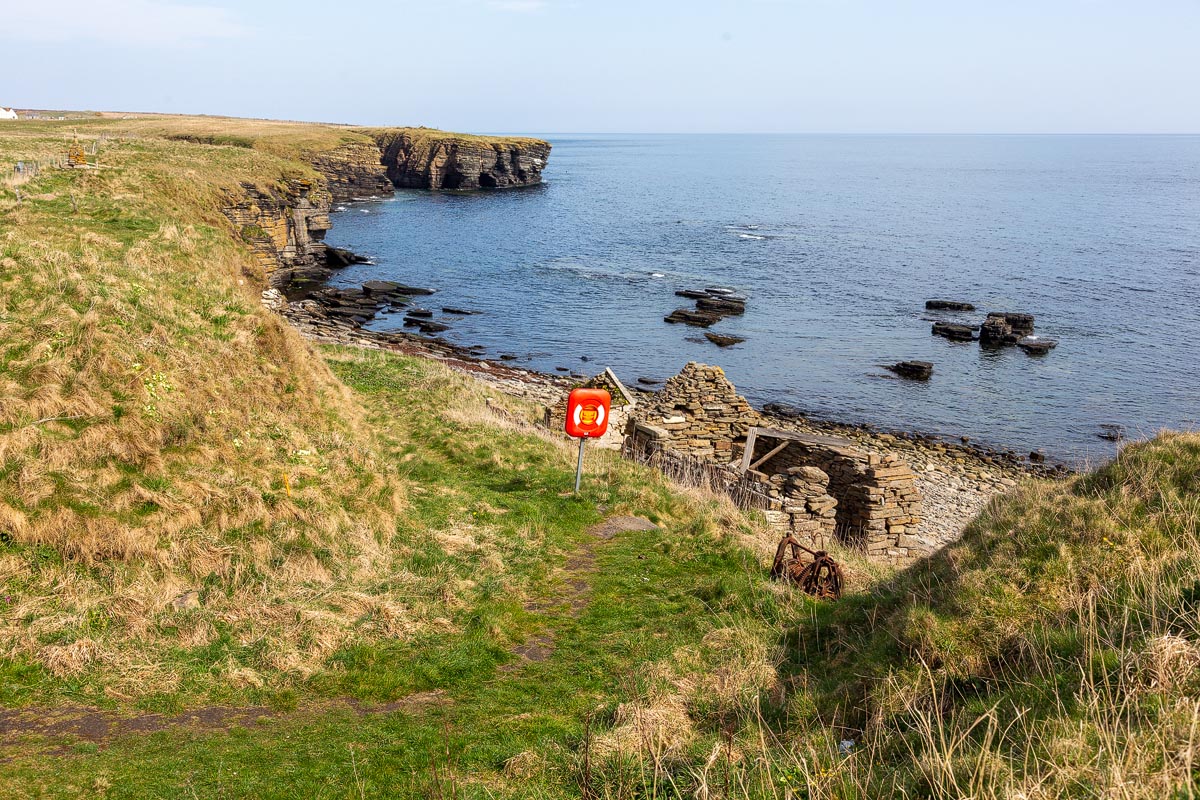 The old Nybster harbour with ruined stone fishing bothy, life ring, and dramatic layered sandstone cliffs