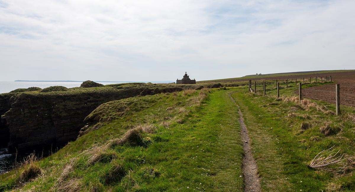The coastal path approaching Mervyn’s Tower at Nybster Broch with dramatic cliff edges to the left
