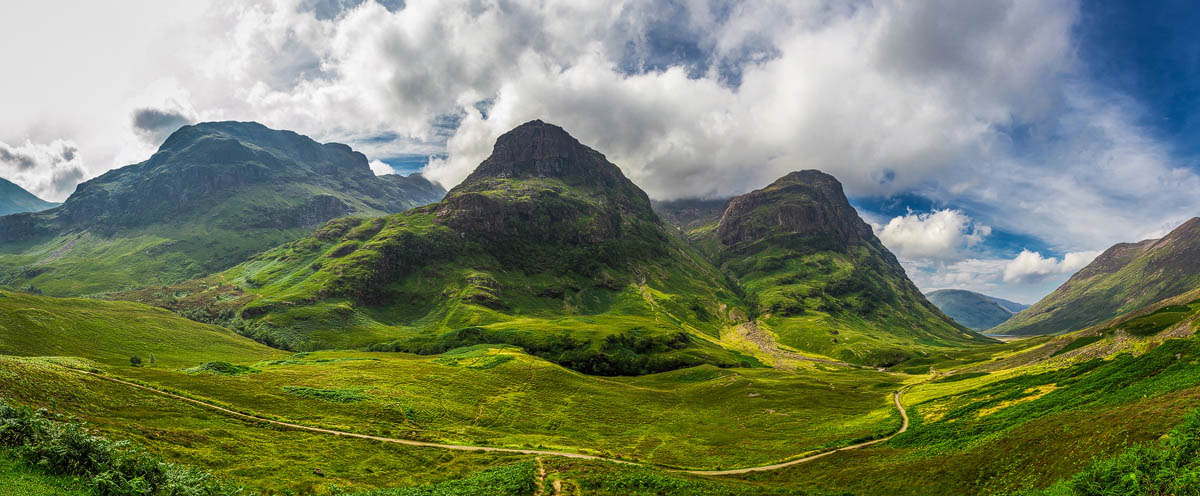 The Three Sisters of Glencoe with dramatic clouds sweeping across the mountain peaks and the valley road below