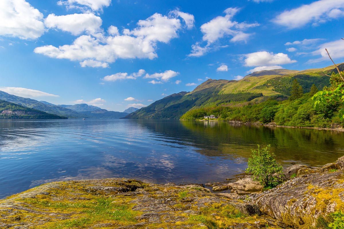 Loch Lomond with calm blue water reflecting the surrounding hills and trees on the shoreline