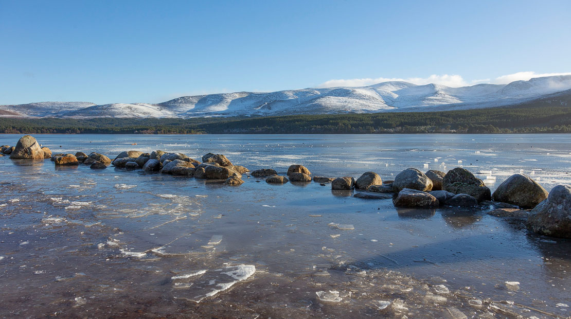 Loch Morlich in winter with ice forming on the shore and snow-capped Cairngorm mountains in the background