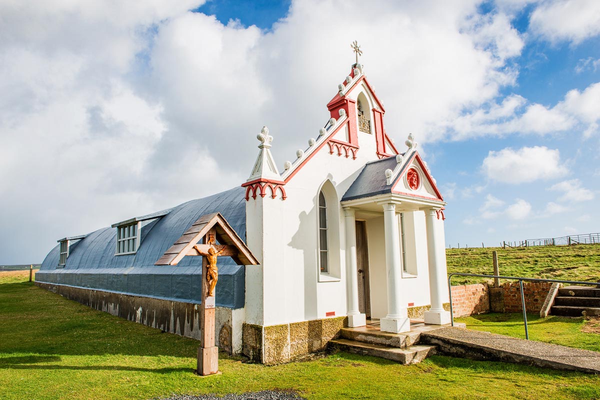 The ornate exterior facade of the Italian Chapel on Lamb Holm, with its Nissen hut structure visible behind