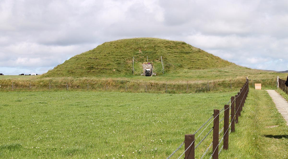 The grass-covered mound of Maeshowe chambered cairn in an Orkney field