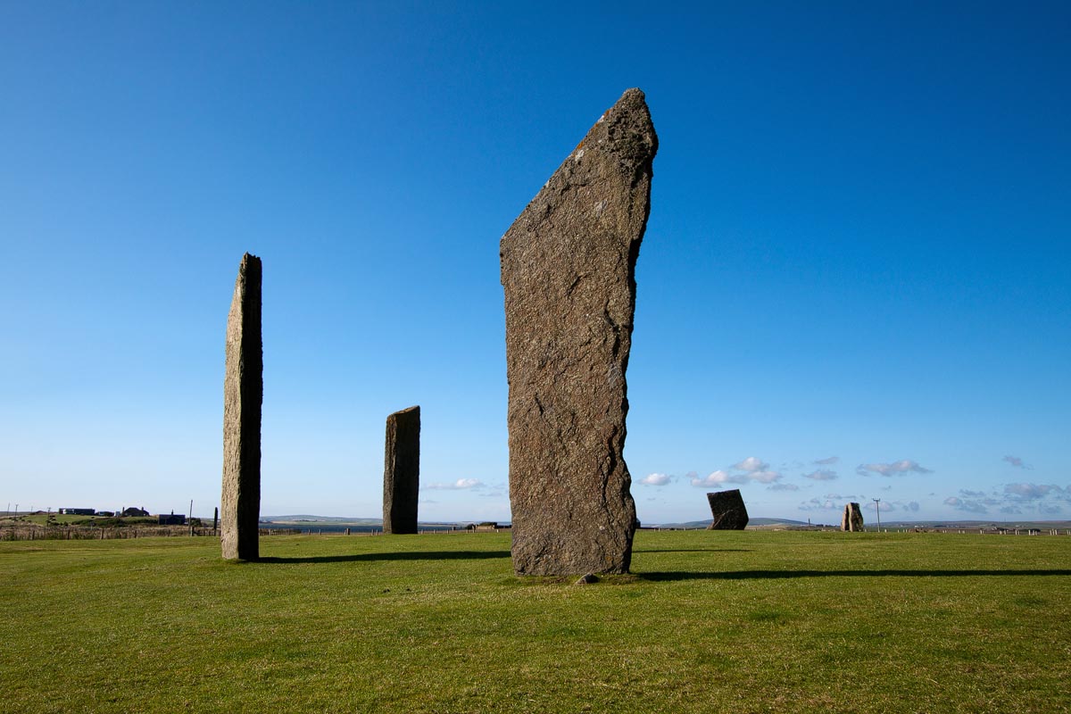 The tall Standing Stones of Stenness with farmland and loch in the background