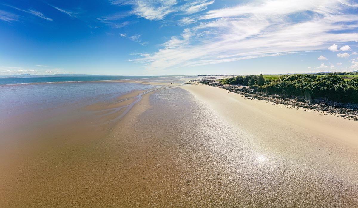 Aerial drone view of Powillimount Beach in Dumfries and Galloway showing vast tidal sands and wooded shoreline