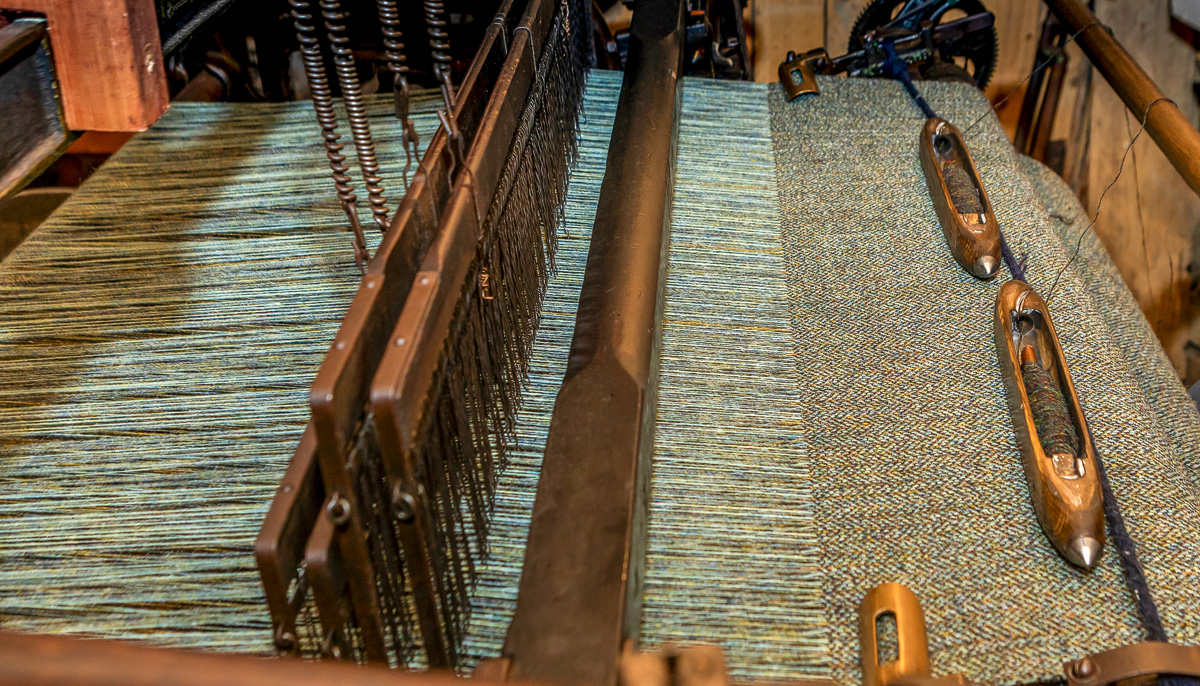 Harris Tweed being woven on a traditional loom, with wooden shuttles resting on the finished cloth