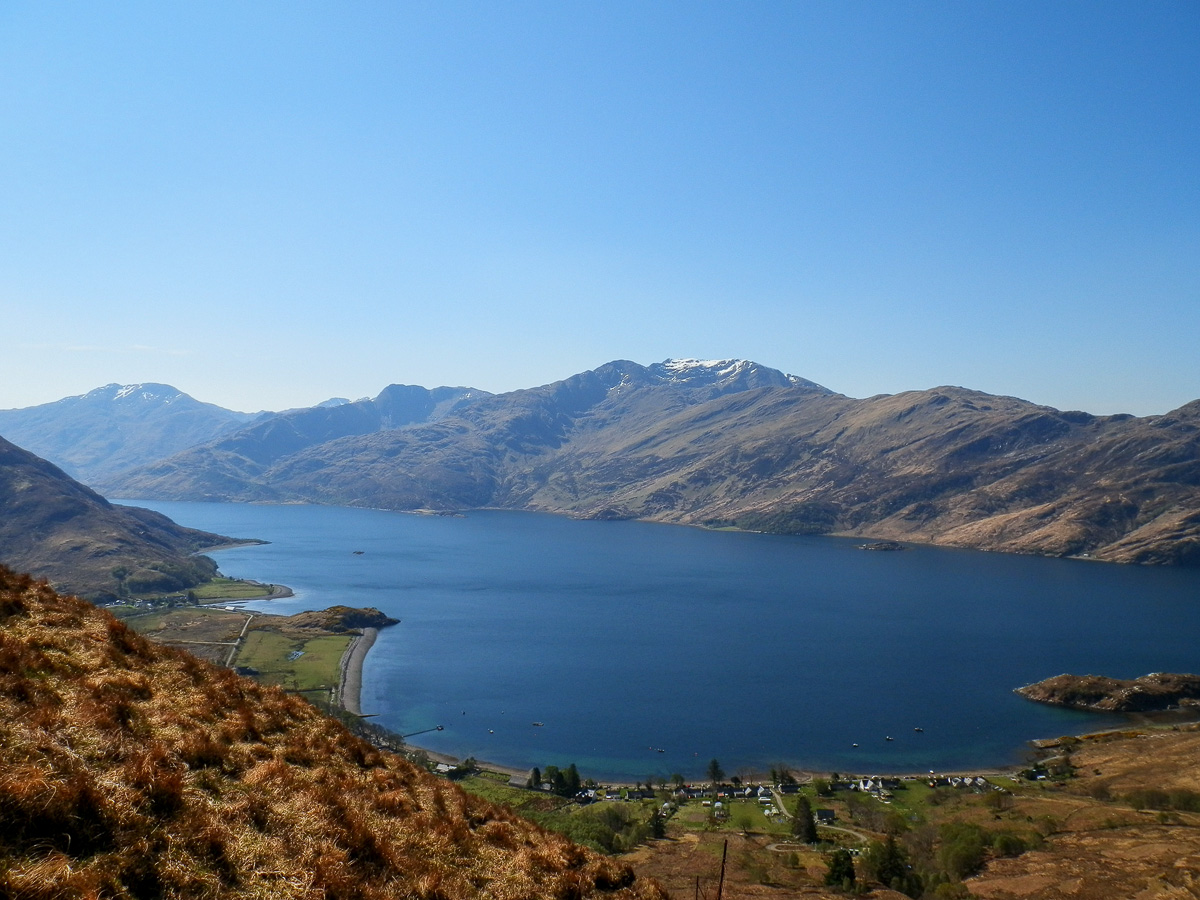 View down over a sea loch and shoreline village to snow-capped mountains on the Knoydart peninsula