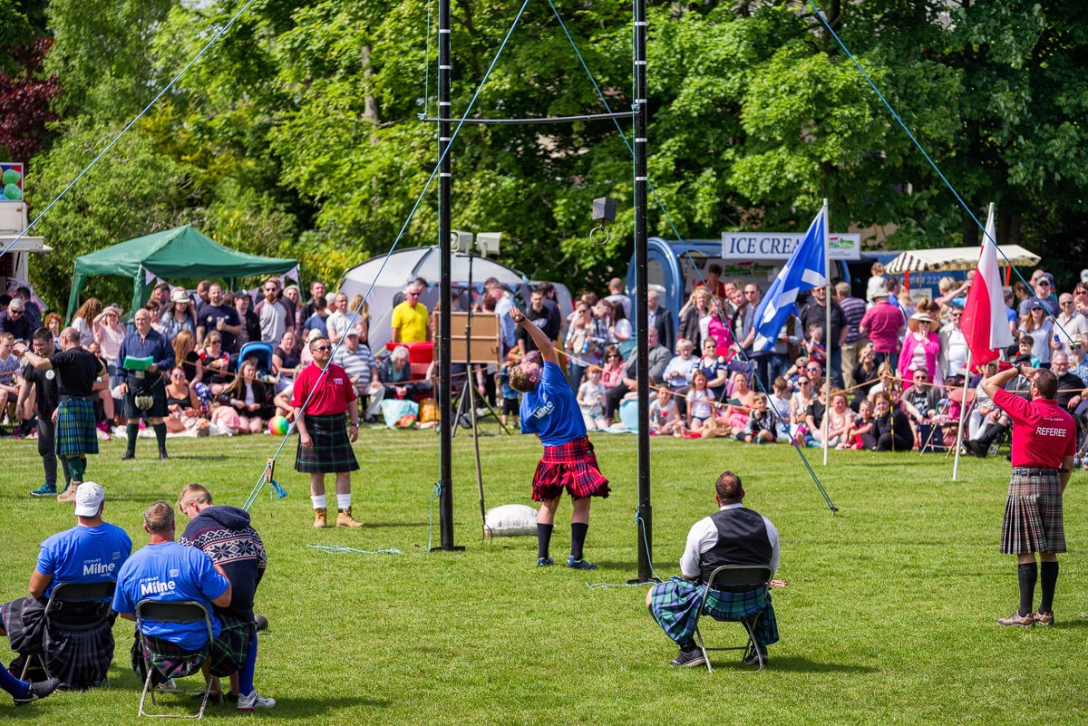 A competitor attempts the weight over the bar at a Highland games event surrounded by officials in kilts and cheering crowds