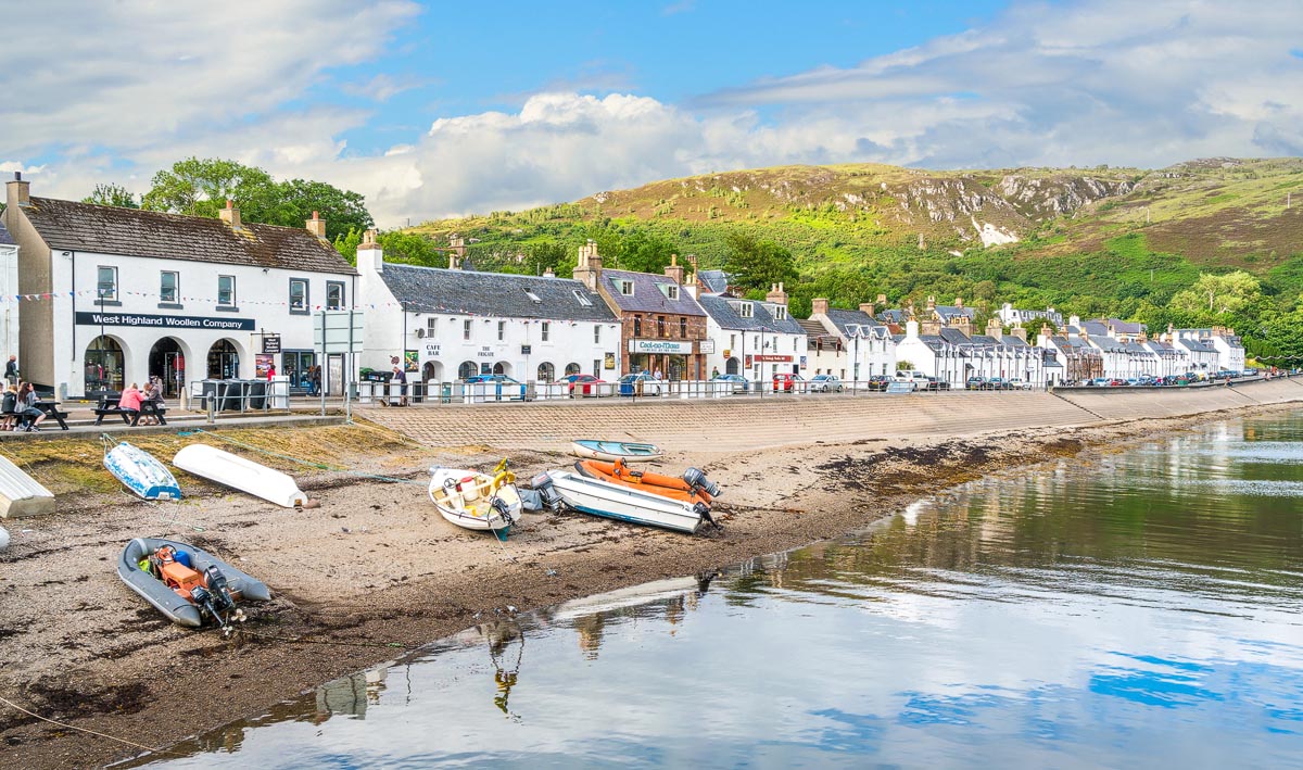 The waterfront at Ullapool with its row of whitewashed buildings, small boats on the shore and hills rising behind