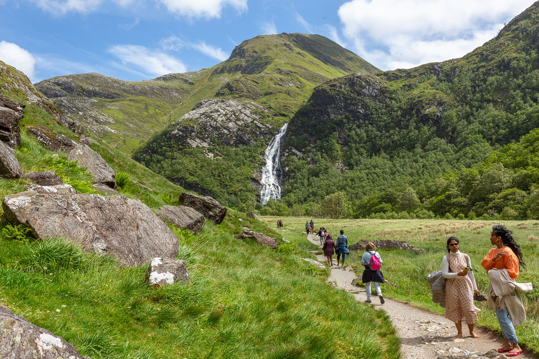 Walkers on the path towards Steall Falls in Glen Nevis with the 120-metre waterfall cascading down the mountainside