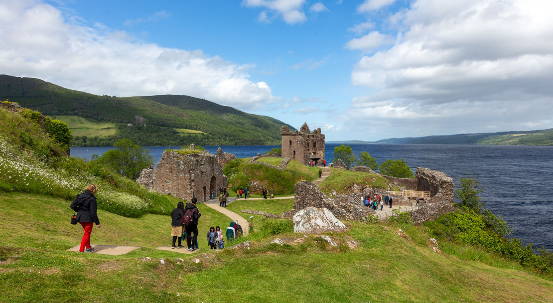 Visitors exploring the ruins of Urquhart Castle on the shores of Loch Ness with the Great Glen stretching into the distance