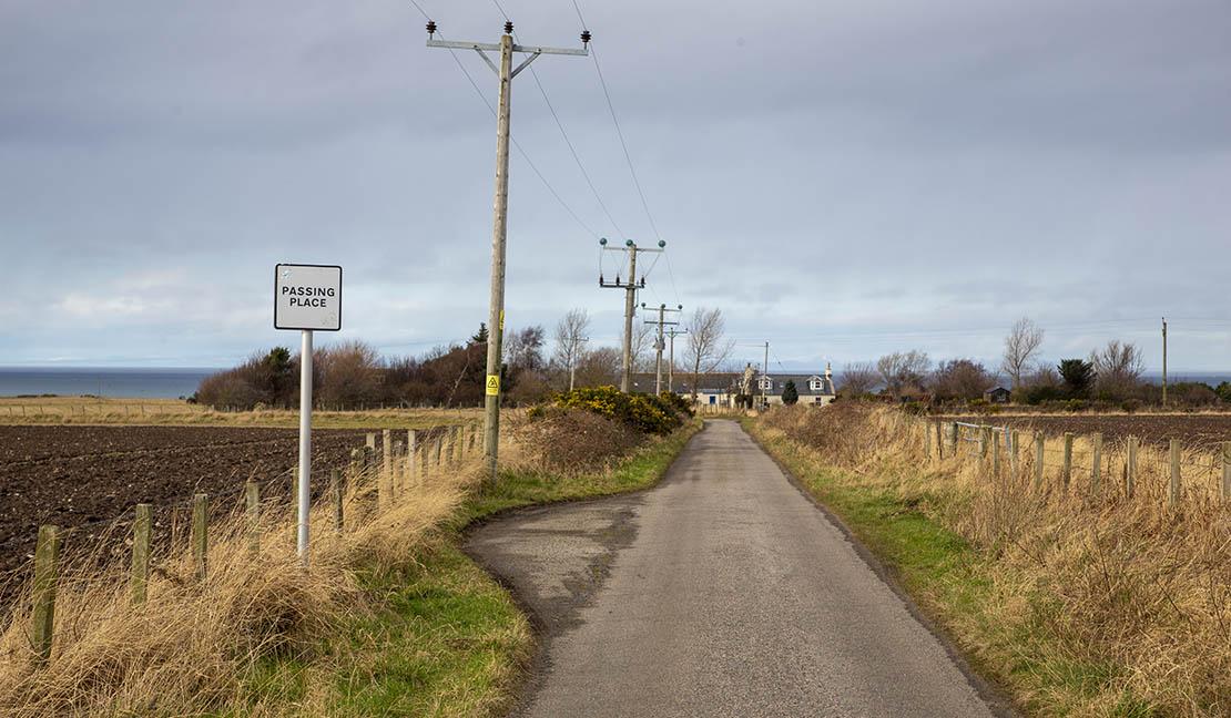 A single-track road with a passing place sign - a common sight on Highland roads with the sea visible in the distance