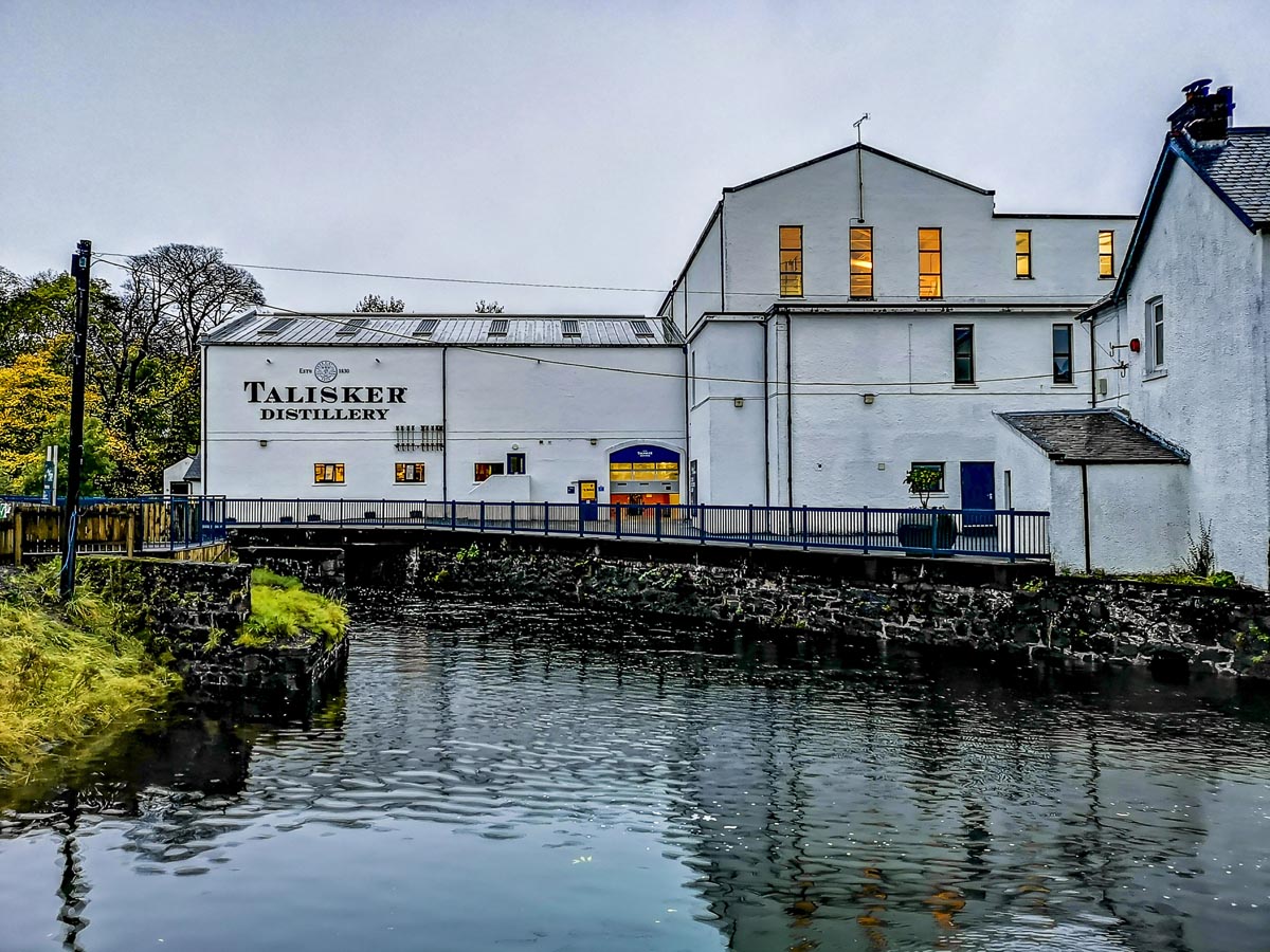 Talisker Distillery on the Isle of Skye viewed from across the water of Loch Harport with warm light glowing from the windows