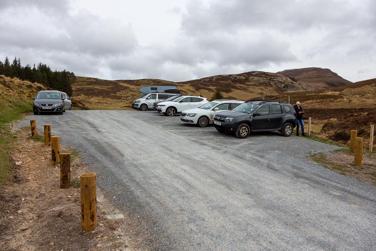 The free car park for the Bone Caves at Inchnadamph with several cars parked and heather-covered hills behind