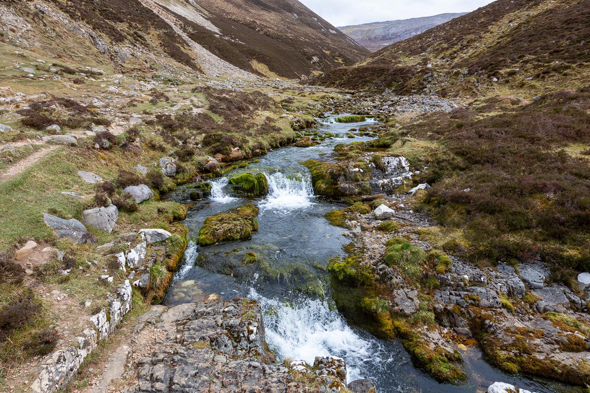 The Fuaran Allt nan Uamh natural spring with water flowing over moss-covered limestone rocks