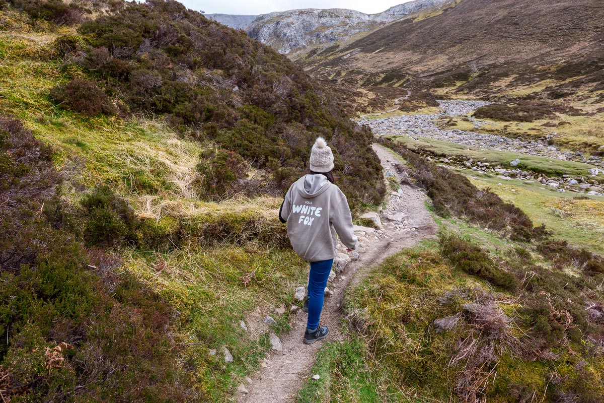 Janette walking along the path with the limestone cliffs of Creag nan Uamh and the dry river bed visible ahead