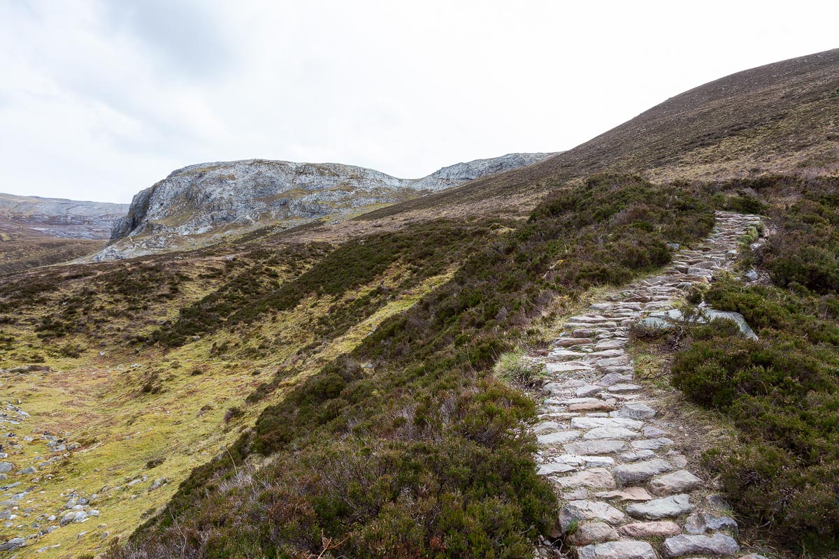 Stone steps climbing steeply up the hillside towards the limestone cliff face of Creag nan Uamh