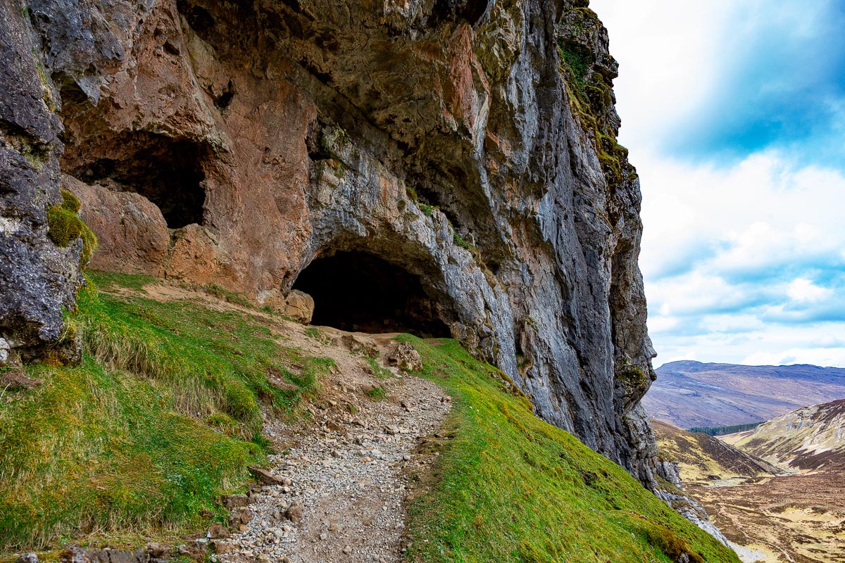 The entrance to one of the Bone Caves at Inchnadamph showing reddish-brown limestone rock with the Allt nan Uamh valley stretching away behind