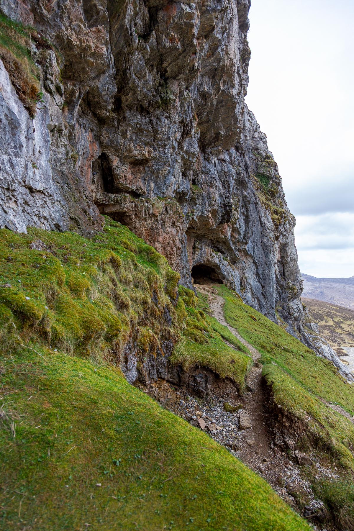 The narrow path traversing the steep grassy slope between cave entrances along the cliff face