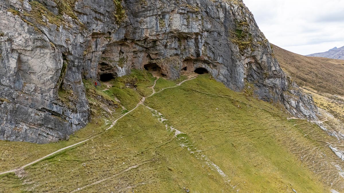 Aerial drone view of the Bone Caves at Inchnadamph showing multiple cave openings in a dramatic limestone cliff face with paths leading up to them