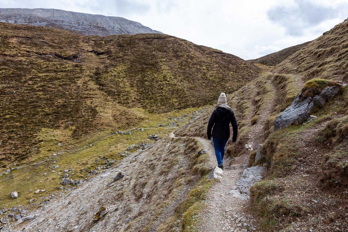 Janette walking along the narrow path beneath the cliff face with the valley stretching away below