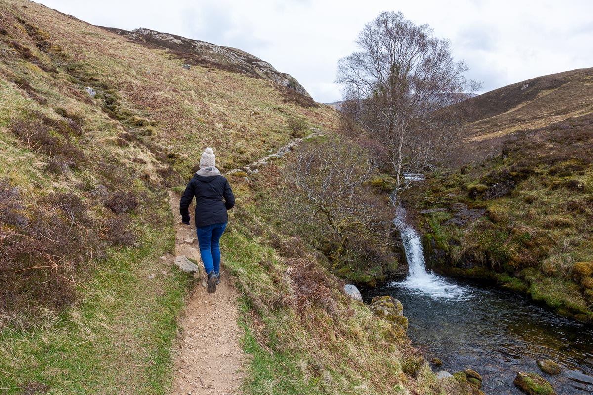 Janette walking along the path beside a waterfall on the Allt nan Uamh burn