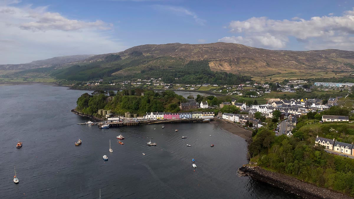 Aerial view of Portree harbour showing the colourful waterfront buildings, moored boats and surrounding hills on the Isle of Skye