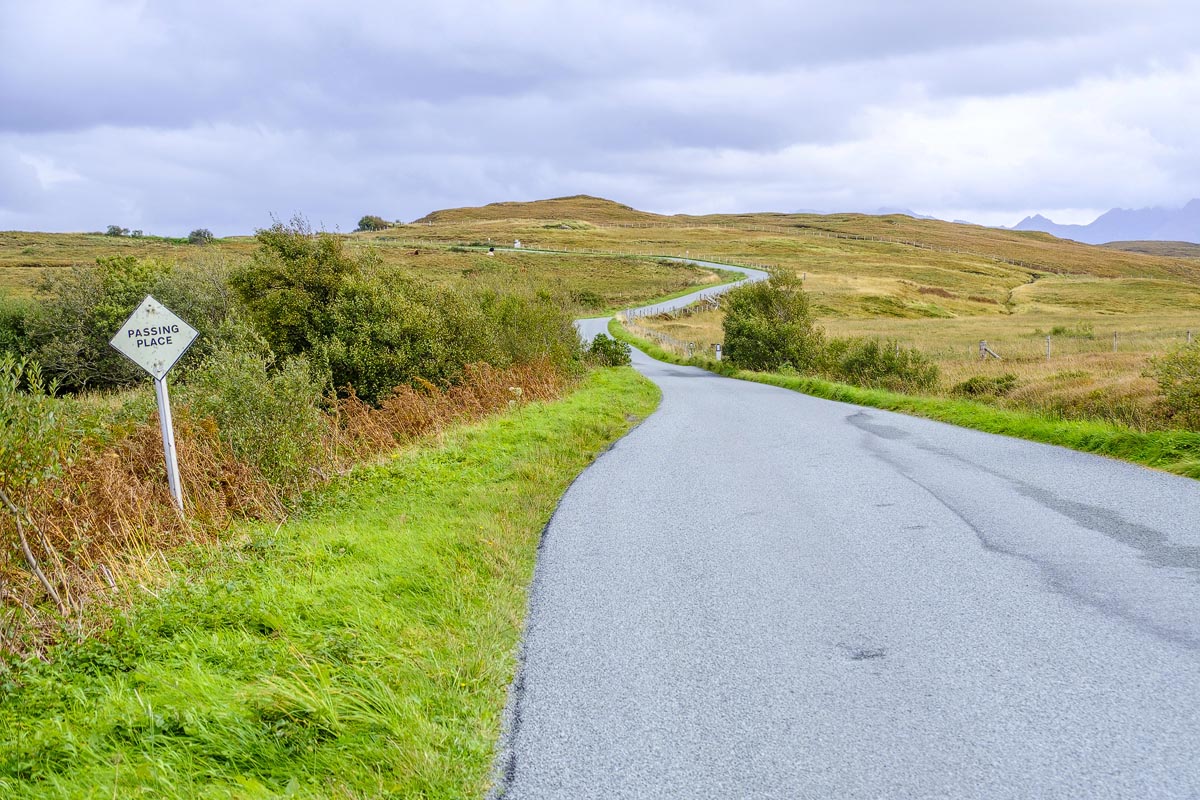 A winding single-track road on the Isle of Skye with a passing place sign and moorland on either side