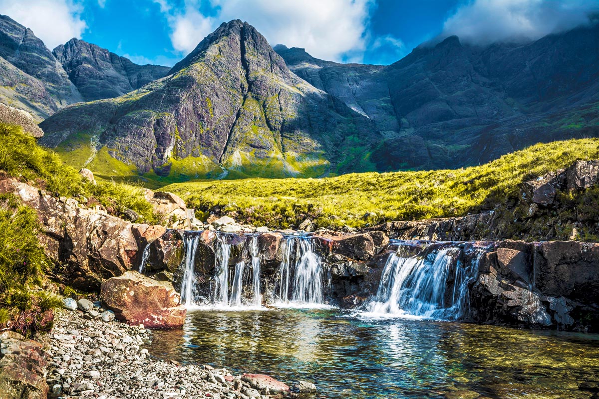 Crystal-clear water cascading over rocks into a turquoise pool at the Fairy Pools with the Cuillin mountains rising behind