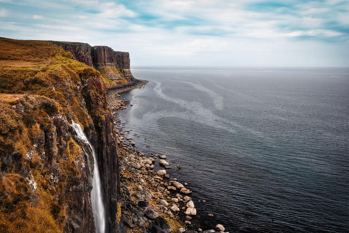 Mealt Falls cascading over sea cliffs into the ocean with the columnar basalt of Kilt Rock visible in the background