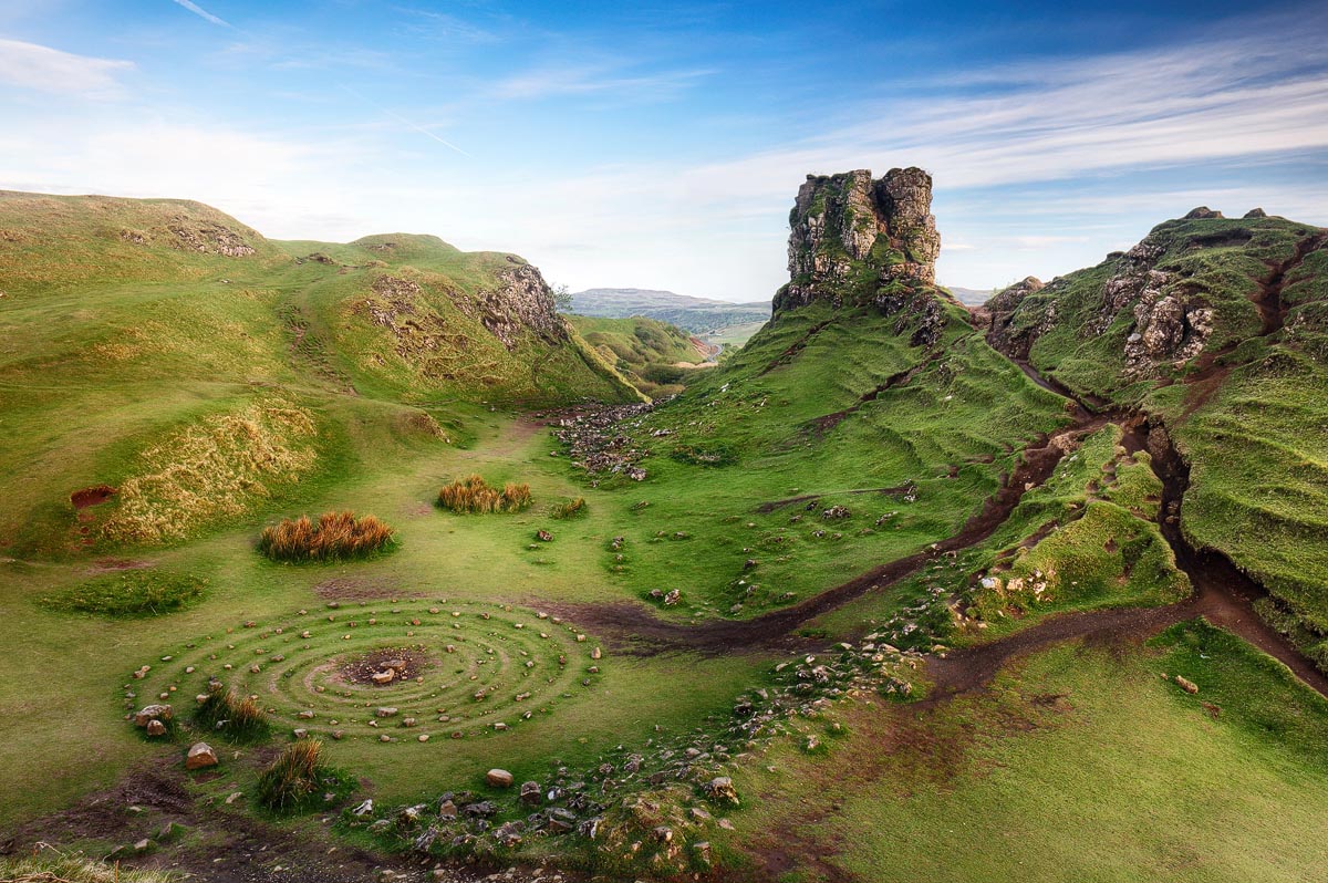 The whimsical landscape of Fairy Glen near Uig with cone-shaped green hills, a stone spiral on the ground and a ruined tower