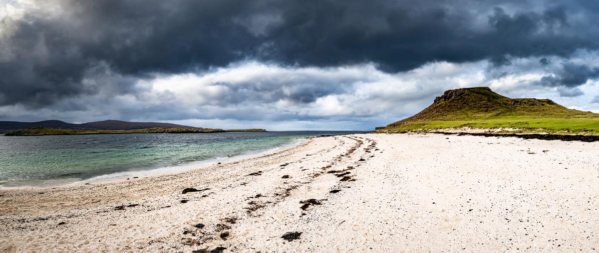 White sand of Coral Beach near Dunvegan with turquoise water and dramatic dark clouds over the headland