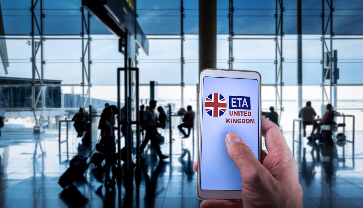 A traveller holding a smartphone showing the UK ETA application in an airport terminal