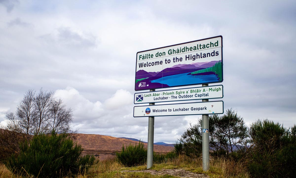 Welcome to the Highlands road sign in Lochaber showing bilingual Gaelic and English text with moorland and mountains behind