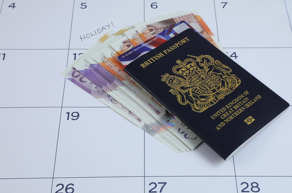 A British passport on a calendar marked with a holiday date alongside banknotes and a UK Global Health Insurance Card